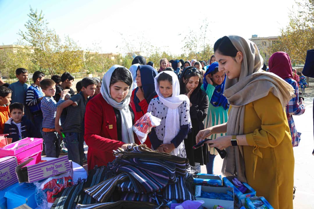 A young woman hands out supplies to girls and children at a community distribution